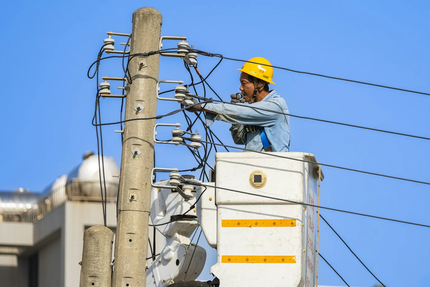 Electrician in a yellow helmet working on power lines from a lift