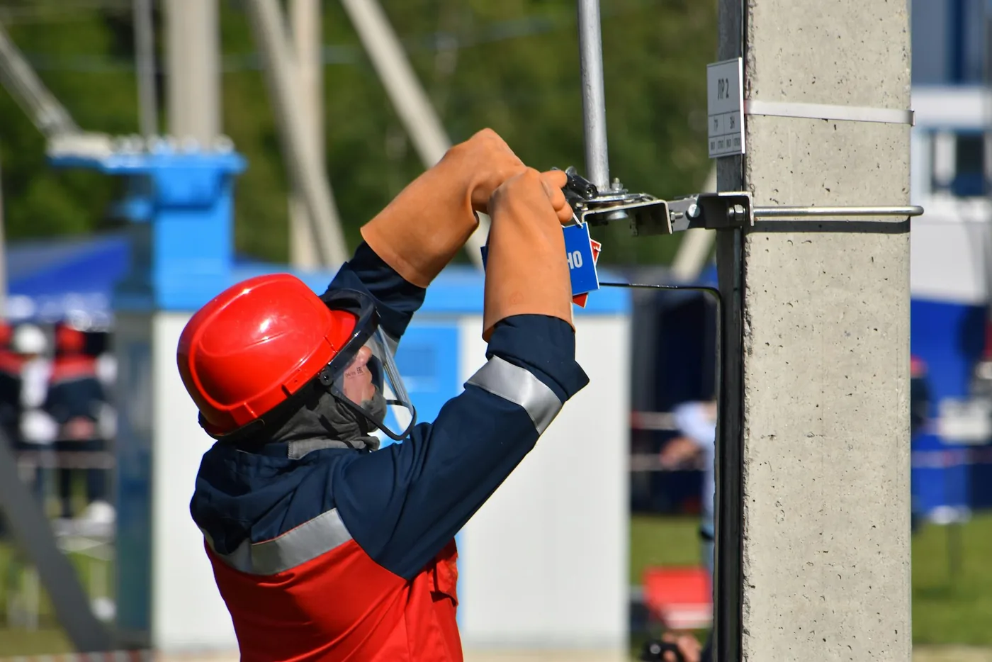 Technician in a red helmet and gloves working at a concrete utility pole