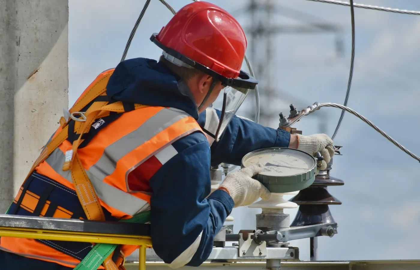 Technician in a red helmet and safety vest working on substation equipment